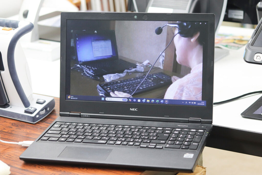 写真:ヘッドセットをつけた人がパソコンに向かっている動画がノートパソコンに表示されている