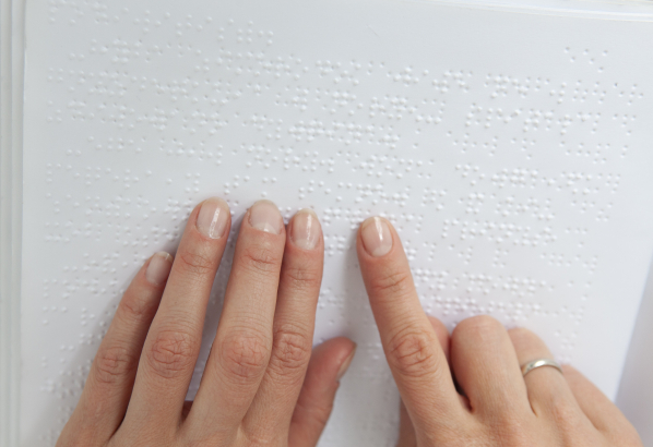 点字が印字された紙の上を、人さし指で触れて読んでいる様子